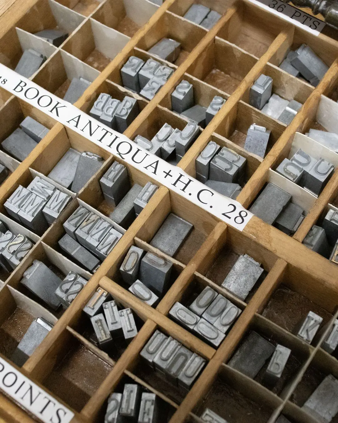 Wooden type case: lead letters sorted in their compartments, with a label reading “Book Antiqua 28 points”.