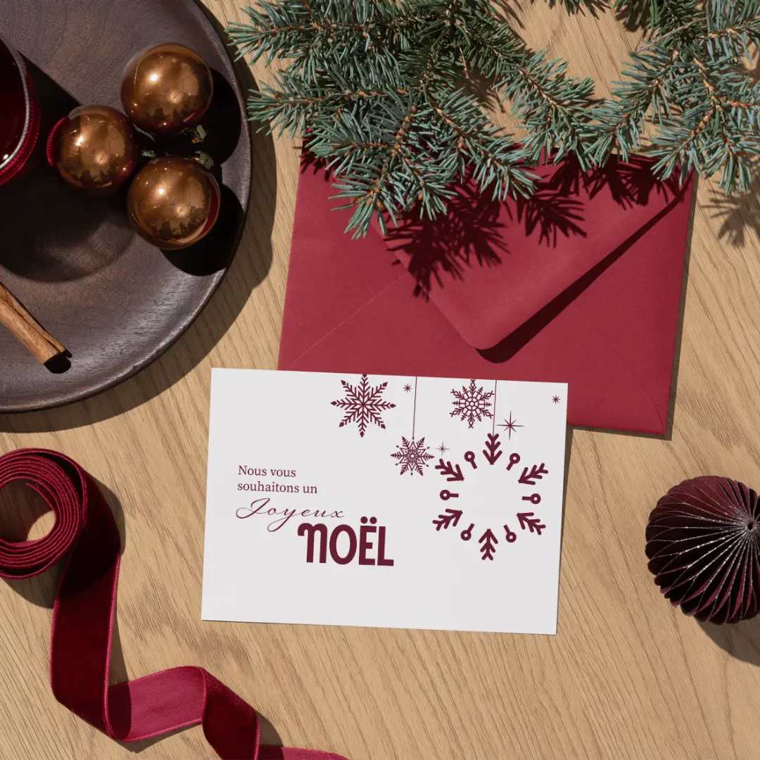 A holiday card with burgundy snowflakes resting on its red envelope, with ribbons and ornaments.