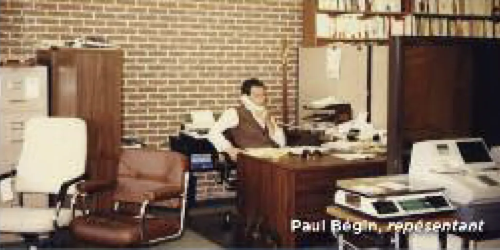 Photo d’archives : un homme au téléphone à son bureau, entouré de classeurs et de machines de bureau.